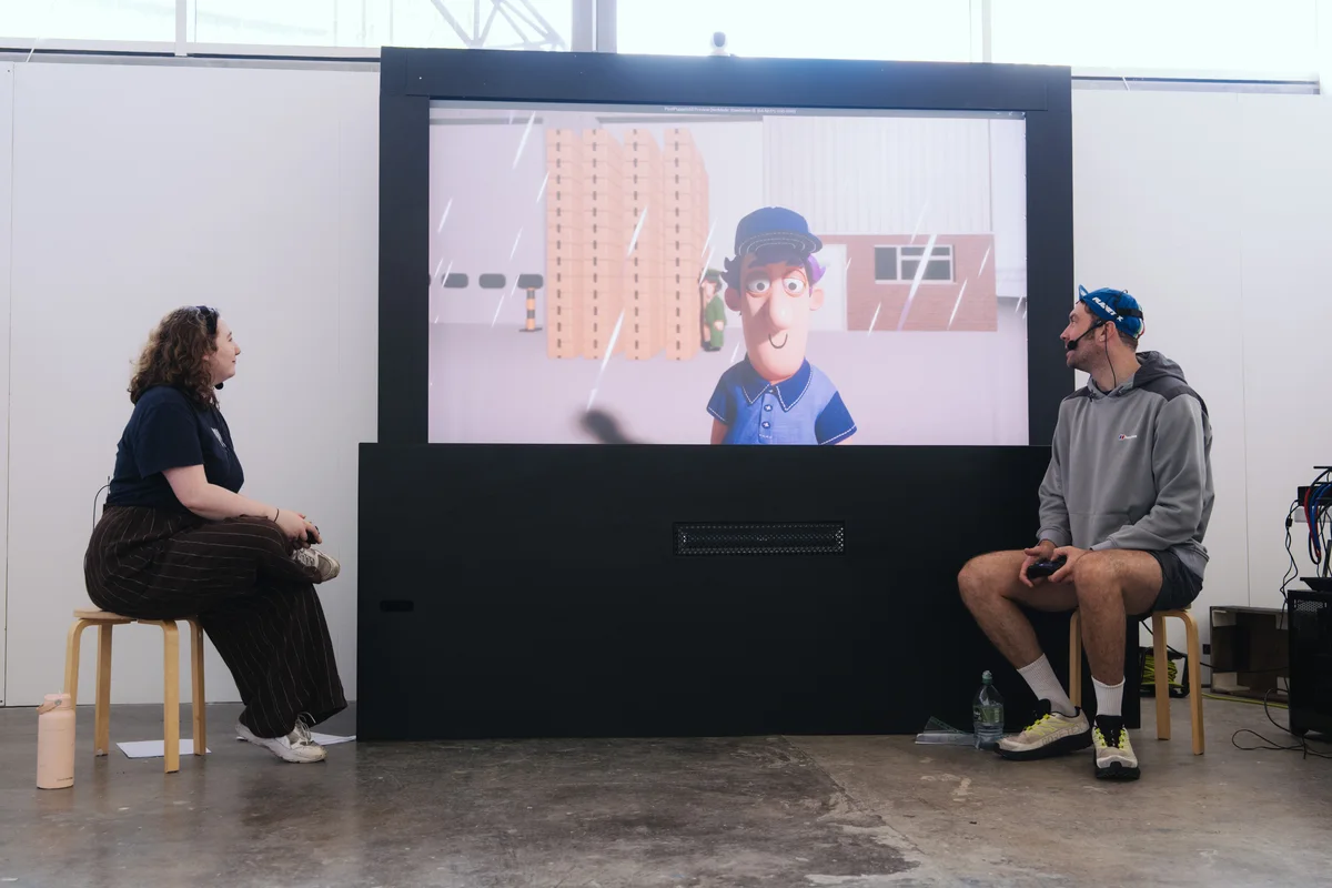 Two performers rehearse with controllers beside a screen showing Matt.